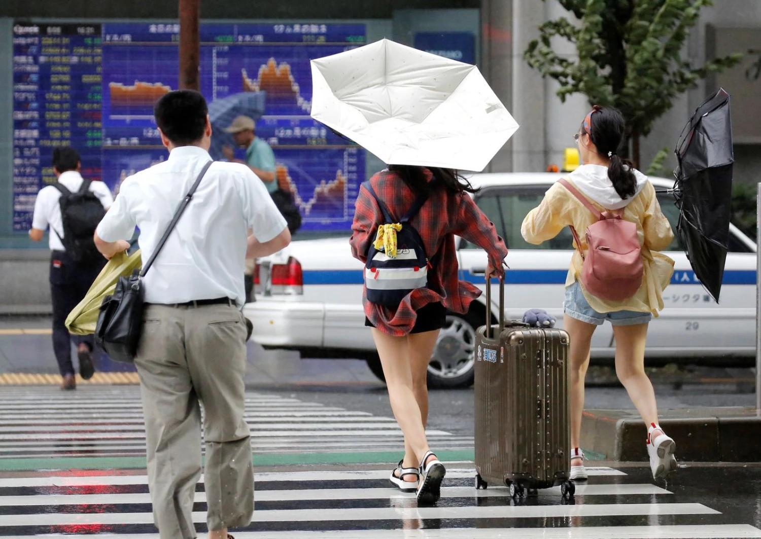 Passersby using umbrellas struggle against a heavy rain and wind in front of an electronic stock quotation board as Typhoon Shanshan approaches Japan's mainland in Tokyo, Japan August 8, 2018.   REUTERS/Toru Hanai