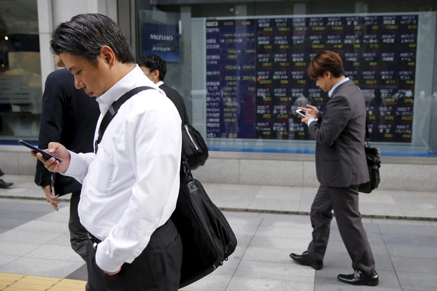 Businessmen look at their mobile phones in front of an electronic stock quotation board outside a brokerage in Tokyo, Japan, October 23, 2015. Asia extended a global stocks rally on Friday after the European Central Bank signaled its readiness to inject more stimulus, helping the dollar scale a fresh two-month peak against the euro. REUTERS/Toru Hanai