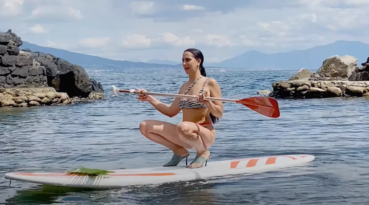 „Zalando“ reklamoje daug kam krito į akį moteris su aukštakulniais ant irklentės. Stop kadras reklamoje. 