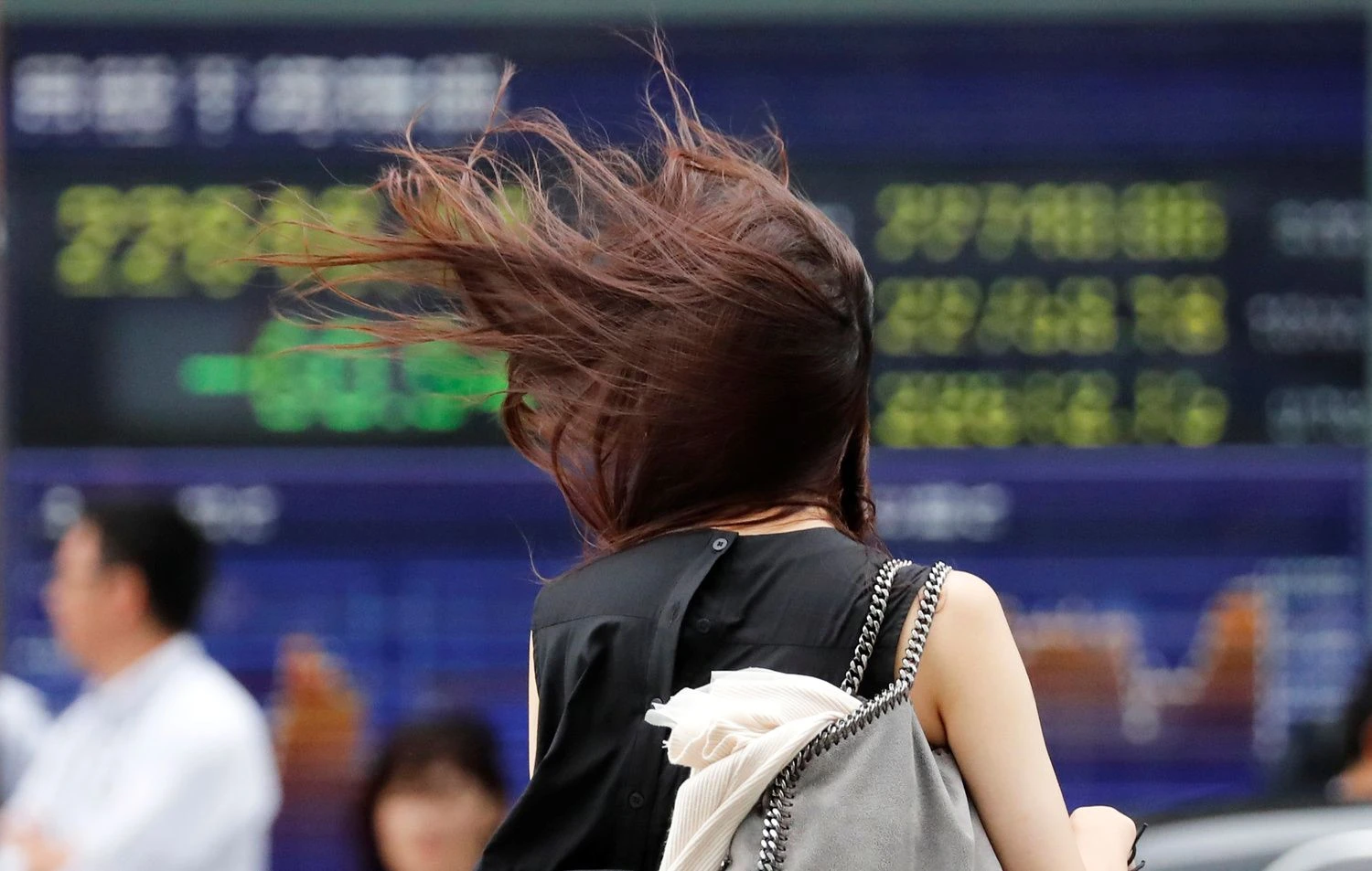 A woman struggles against strong wind caused by Typhoon Jebi, in front of an electronic stock quotation board in Tokyo, Japan, September 4, 2018.   REUTERS/Toru Hanai