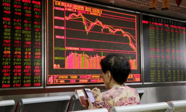 An investor checks stock information on her mobile phone in front of a board at a brokerage office in Beijing, China July 6, 2018. REUTERS/Jason Lee